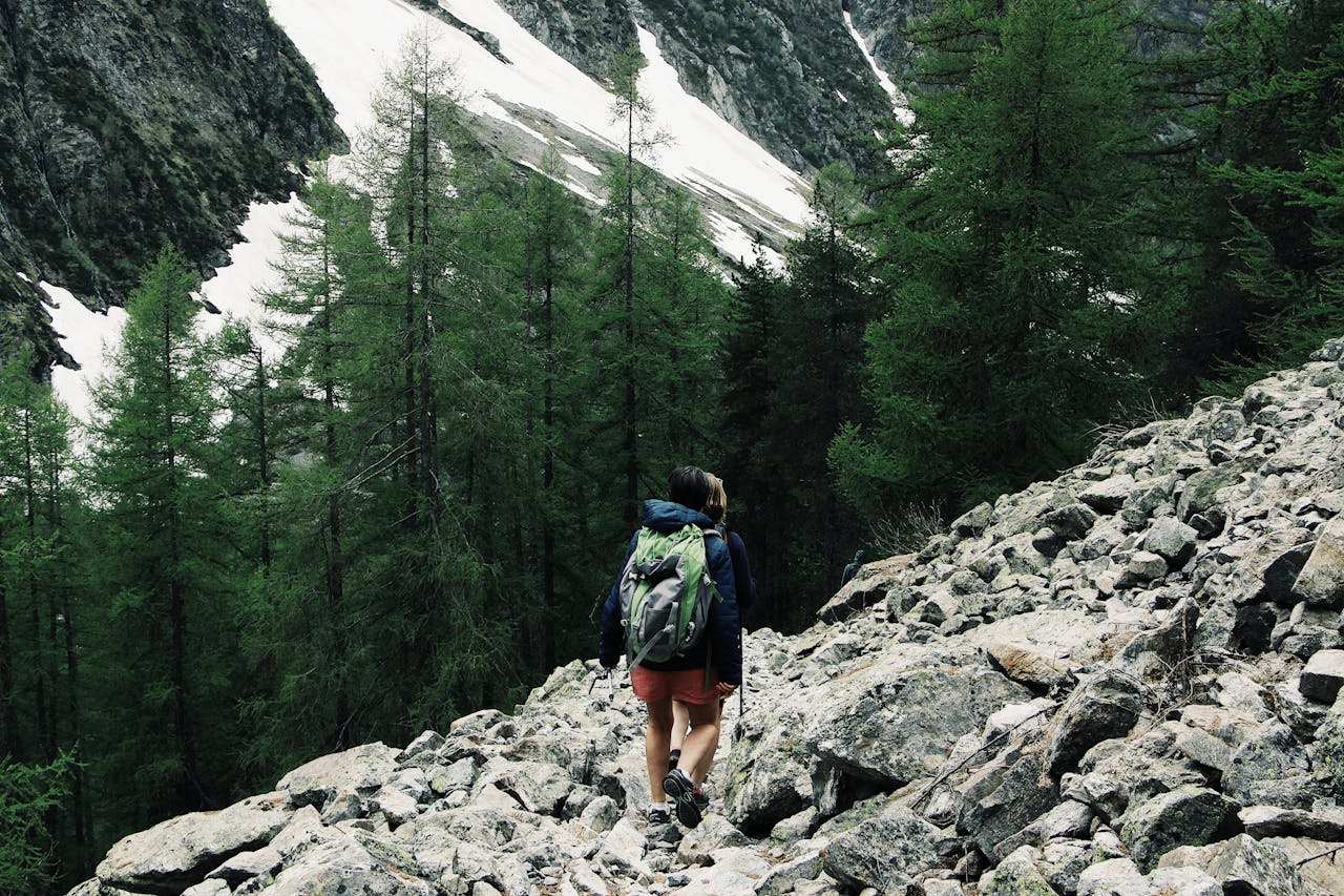 why-choose-us Wanderer mit Rucksack auf felsigem Pfad mit schneebedeckten Gipfeln.